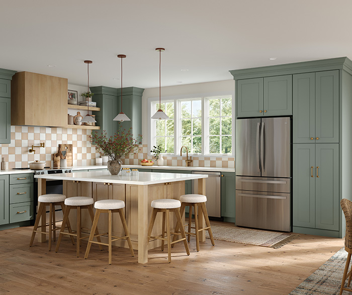 Modern farmhouse kitchen featuring sage green cabinets, large wood island with white countertop, stainless steel refrigerator, and warm wood flooring.